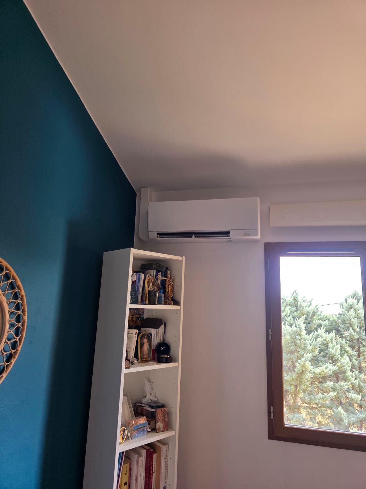 Split mural de climatisation au-dessus d’une bibliothèque, goulotte de liaison suivant l’angle du mur
